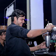 One of my skilled mixologists pouring a freshly shaken cocktail. The tattoo on his arm, 'Maa', adds a personal touch, reflecting the heart my team puts into their work.