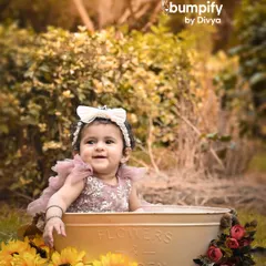 A sweet smile from the baby girl in her outdoor tub session. The natural greenery and soft sunlight create a beautiful, dreamy atmosphere.
