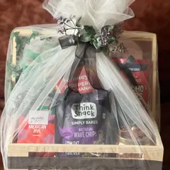 This engagement gift hamper, filled with a variety of gourmet snacks, is beautifully wrapped in white net with a black ribbon and floral accent. The wrapping adds an extra layer of luxury and anticipation.
