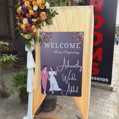 A personalized welcome stand for a wedding. The custom sign with the couple's names is set against a backdrop of peach-coloured fabric and topped with a large, beautiful floral arrangement.