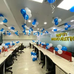 A full office space decorated for an inauguration ceremony, with blue and white balloon bunches and a "Happy Inauguration" foil banner.