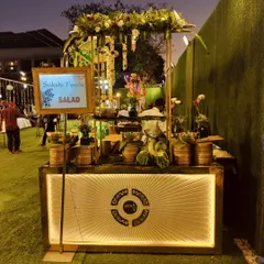 An illuminated salad station set up for an evening wedding on a lawn, designed to be both a food counter and a beautiful piece of event decor.
