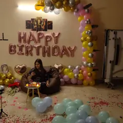 Here is one of my decorations in a real home setting. This surprise birthday party setup includes rose gold foil balloons, a colorful balloon half-arch, and scattered petals to create a festive atmosphere.