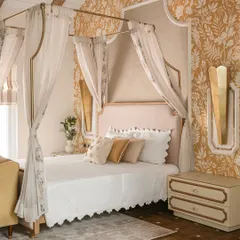 For this bedroom, we created a sanctuary that blends vintage romance with contemporary calm. The custom four-poster bed, draped in sheer fabric, becomes the centerpiece, complemented by warm golden wallpaper and bespoke nightstands, crafting a visual lullaby for the senses.