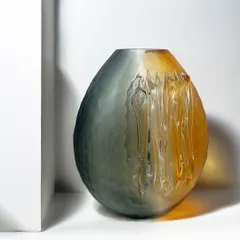 A striking blend of smoky grey melting into warm amber, this blown glass vase is a true conversation starter. Its organic oval form and textured finish make every angle unique.