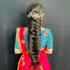 This is a very traditional, thick, and long bridal braid, perfect for a classic wedding look. The hairstyle is neat and elegant, finished with a simple gold hair accessory at the top.