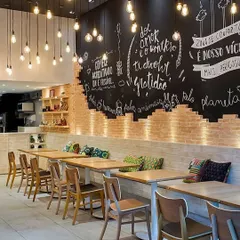 For this cafe, we created a warm, industrial-chic vibe using an exposed brick feature wall with custom chalkboard art. The space is lit with hanging Edison bulbs, and the seating arrangement with simple wooden tables and chairs provides a cozy, rustic setting for patrons.