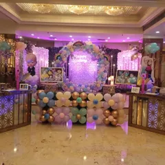 A wide view of a lavish birthday party stage. The setup includes a central circular balloon wreath, two shimmer walls, and multiple character cutouts like Boss Baby and Frozen's Elsa.