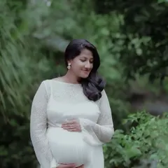 A gentle and introspective portrait. The soft focus on the background greenery makes the mother-to-be and her peaceful expression the center of attention.