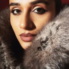 An extreme close-up beauty shot, where the texture of the faux fur coat frames the model's face. The focus is on the sharp, winged eyeliner and the soft, neutral lip.