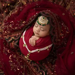 A close up of this precious baby, showcasing the delicate jewelry and the luxurious red and gold fabric that envelops her. This is a modern heirloom in the making.