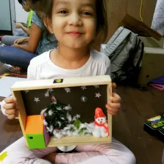 A proud student shows off her completed Christmas diorama. This project involved building a scene with a snowman and tree, and wiring a simple circuit to make it light up.
