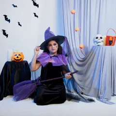 A medium shot of the witch costume, allowing customers to see the details of the purple cape and hat. The themed props like the jack-o'-lantern and skull add context and make the photo more engaging for seasonal marketing.