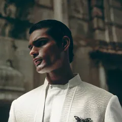 A strong profile shot highlighting the sharp cut of the jacket and the subtle insect brooch, a key styling detail for this Dhruv Vaish look.