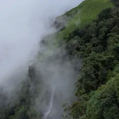 A glimpse of a waterfall cascading down the misty green hills along the Bandaje Arbi trek. This trail is a paradise for waterfall lovers.