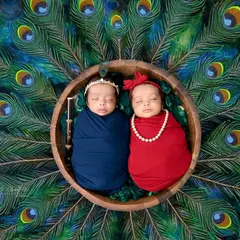 Double the love, double the charm. These precious twins are styled as little Radha and Krishna, nestled in a bowl against a backdrop of peacock feathers. Capturing twins is a special art, and this image shows the divine bond they share from the very beginning.