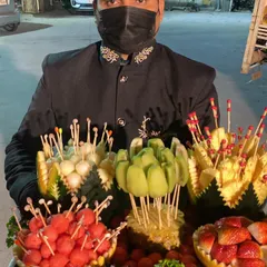 Our staff presenting an elaborate fresh fruit platter. The fruits, including watermelon, muskmelon, kiwi, and pineapple, are intricately carved and arranged on skewers for easy and elegant snacking.