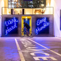 We transformed an old warehouse into an energetic office space, using neon signs like 'Work Hard Stay Humble' to motivate and inspire. The open-plan design includes unique features like an indoor cycling track, blending industrial grit with a playful, modern spirit to create a workspace that's anything but ordinary.