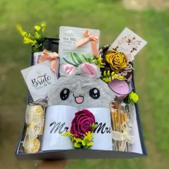 A complete view of our "Bride to Be" hamper. This gift box is packed with goodies to help her relax and celebrate, including "Mr." and "Mrs." mugs, a face mask, a scented candle, makeup brushes, and a cute fluffy pouch.