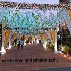 A bright and welcoming entrance for a daytime or evening event. The walkway is lined with yellow and white drapes, fairy lights, and a ceiling of hanging white flowers.
