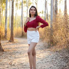 A full-length portrait taken during a golden hour shoot in the woods. The warm light filtering through the trees creates a beautiful, serene atmosphere that highlights the model's graceful pose.