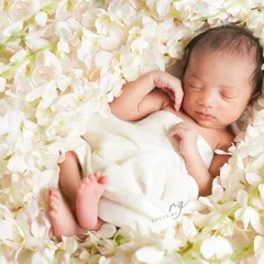 A newborn rests peacefully amidst white flowers, a classic and timeless setup that emphasizes their delicate features. We create these serene scenes at our studio or your home.