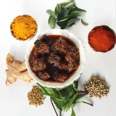 My traditional Mutton Pickle, surrounded by the fresh ginger, turmeric, and spices I use to make it. This is a bold, rich pickle made with high-quality meat.