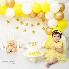 A sunny and cheerful first birthday celebration. This setup features a bright yellow balloon arch, a sweet teddy bear, and a delicious cake, creating a perfect scene for a happy one-year-old girl.