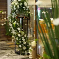 Elegant floral stands for a Roka ceremony. Cascading white flowers on black metal stands, paired with wooden candle holders, create a sophisticated and welcoming entrance.