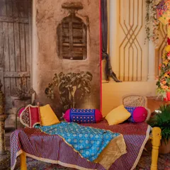 A traditional seating area for a Punjabi-themed event. The charpai is draped with colorful fabrics like Phulkari, and the backdrop is designed to look like the wall of a village home, creating an authentic and rustic feel.
