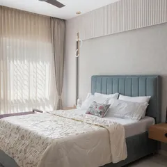 This bedroom uses a softer, pastel blue palette for the headboard, complemented by light wood tones and ample natural light to create a serene and airy retreat.