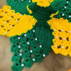 A close-up view of the detailed crochet and pearl work on the green and yellow floral dress. I carefully select each moti to complement the colors of the yarn.