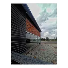 An angled view of the commercial building, highlighting the contrast between the dark corrugated metal cladding and the warm, patterned terracotta screen. This juxtaposition of materials is a key feature of the building's architectural identity.