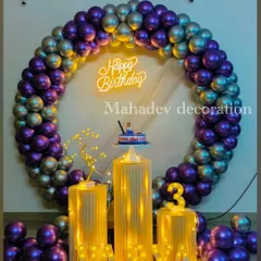 A sophisticated birthday setup with a full circular arch of metallic purple and silver balloons. The decor is enhanced by pedestals wrapped in lights and a 'Happy Birthday' neon sign.