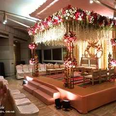 This is an example of a beautiful indoor Vidhi Mandap. The combination of a dense floral canopy with hanging white flowers and elegant gold structures creates a sacred and luxurious atmosphere within a banquet hall.