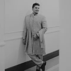 A classic black and white portrait of the groom leaning against a wall. His relaxed pose and confident smile create a timeless and effortlessly cool image.
