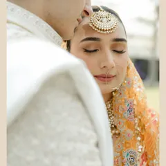 A moment of pure serenity. This intimate close-up focuses on the bride's peaceful expression as the groom kisses her forehead. Her look is styled with a statement maang tikka and soft, natural makeup.