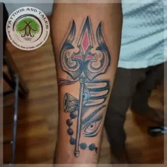 A powerful Trishul tattoo on the forearm, combined with a Rudraksha and the third eye of Lord Shiva. The red accent on the Trishul adds a focal point to the black and grey design.