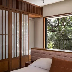 A closer look at the master bedroom's custom wardrobes and the expansive window. The warm wood tones and soft, filtered light contribute to the room's calming, meditative atmosphere.