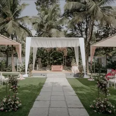 A wider view of our elegant garden wedding setup, showing the main stage, guest seating with white Chiavari chairs, and soft pink drapery on the surrounding canopies. The open, airy design blends seamlessly with the natural landscape.