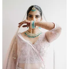 A striking bridal portrait of Karishma. The way she uses her hand and the veil to partially cover her face creates a sense of mystery and highlights her expressive eyes.