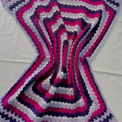 The beautiful wave effect created by this striped blanket in shades of purple and pink. The pattern is a simple variation of the granny stitch, creating a modern and eye-catching design.