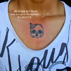A small skull and butterfly tattoo on the collarbone, a unique and minimalist piece.