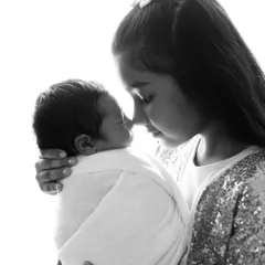 Another beautiful black and white shot capturing the gentle bond between an older sister and her newborn sibling. Her expression is full of care and wonder.