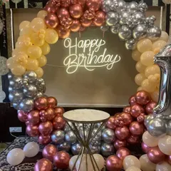 A stylish birthday balloon ring using a mix of rose gold, peach, and silver chrome balloons, with a central pedestal for the cake.