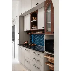 To brighten this kitchen, I used light-colored laminate for the cabinets. A teal-colored subway tile backsplash in a herringbone pattern adds a contemporary twist, while a special nook showcases cherished brass items.