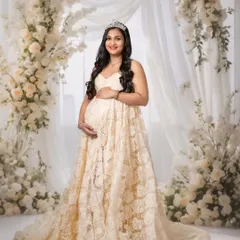 A classic portrait of a mom-to-be in a beautiful lace gown, wearing a tiara against a wall of white flowers for a truly royal feel.