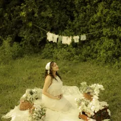 A moment of pure bliss. The mother-to-be soaks in the sun during her picnic-themed shoot, with a clothesline of baby clothes in the background adding a sweet, narrative touch.