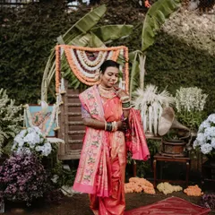 A full-length portrait of a bride in her pink nauwari saree, set against a backdrop of traditional decor. This shot captures the complete bridal look and the festive atmosphere.