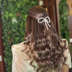 A beautiful and simple hairstyle for a daytime event. Soft waves are pulled back with a delicate pearl bow accessory, creating a look that is both elegant and trendy.
